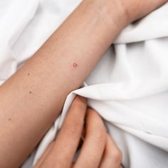 a woman's arm with a tiny heart tattoo on it, while laying in bed