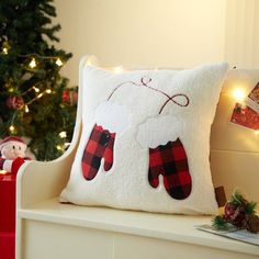 a white pillow with red and black mittens on it next to a christmas tree