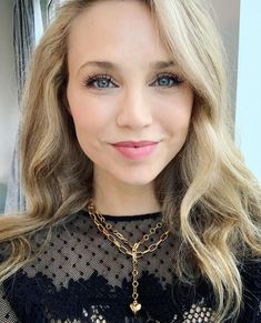 a woman with blonde hair wearing a black top and gold chain necklace smiling at the camera