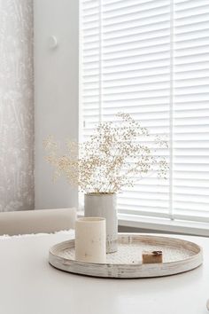 a white table with some flowers in a vase on it and a window behind it