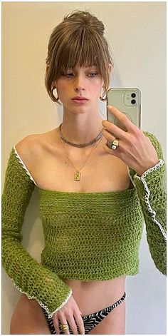 a woman taking a selfie in front of a mirror wearing a green knitted top