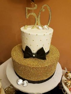 a 50th birthday cake decorated with gold glitter and a bow tie on top for someone's 50th