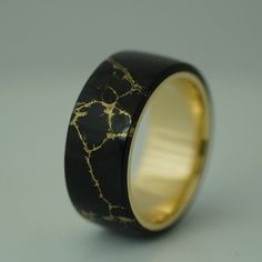 a black and gold wedding ring with an intricate design on the inside, sitting on a gray surface