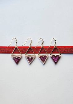 three pairs of earrings are hanging from a red ribbon on a white surface, one is purple and the other is pink