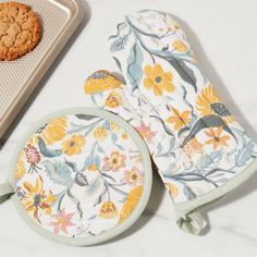 an oven mitt, cookie and baking sheet on a white countertop with flowers