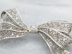 Add a touch of elegance and whimsy to any outfit with this bow brooch. The delicate filigree detailing and sparkling European Cut diamond make this brooch a timeless statement piece. Perfect for any occasion!Metal: 14K White GoldGem: European Cut Diamond .10 Carats, SI1 in Clarity, I in ColorGem Measurements: 3.2 mm, RoundMeasurements: 44 x 23 mmMarks: "X14K" Stamped on the pin guard Exquisite Diamond Accented Brooches For Wedding, Exquisite Wedding Brooches With Diamond Accents, Formal Diamond Brooch With Intricate Design, Formal Diamond Brooches With Intricate Design, Classic Wedding Brooches With Intricate Design, Heirloom Wedding Brooches With Intricate Design, Elegant Brooch With Diamond Accents As Gift, Elegant Diamond Accented Brooch Gift, Elegant Diamond Accented Brooches As Gifts