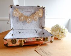 an open suitcase sitting on top of a wooden table next to flowers and a tag