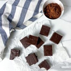 several pieces of chocolate next to a bowl of cocoa on a white surface with blue and white striped towel