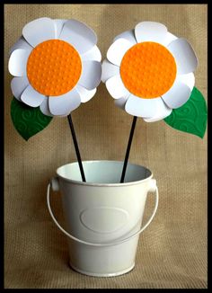 two paper flowers in a bucket with green leaves