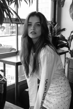 a woman sitting in front of a window next to a potted plant