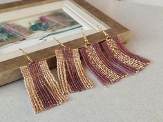 three pairs of beaded fringe earrings on a table next to a framed photograph and wooden frame