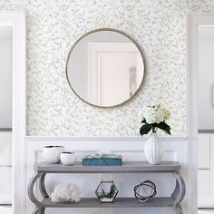 a console table with a mirror and vase on it in front of a wallpapered background