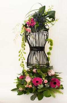 a birdcage filled with flowers and greenery on top of a white surface