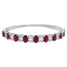 This 18k white gold bangle features 4.49 carats of rubies and emerald-cut diamonds composed of baguette and round diamonds. It is secured with a box clasp and figure-8 safety closures. This bangle is designed to be worn individually or combined with other bracelets for a layered look. Ruby - 4.49 Cts Diamond- 1.02 Cts All Diamonds are G-H/SI