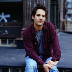 a man sitting on the ground with his hands in his pockets and looking at the camera