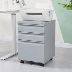 a white printer sitting on top of a desk next to a vase filled with flowers