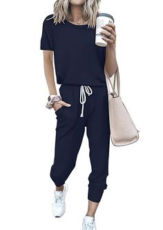 a woman in black jumpsuits holding a coffee cup and a handbag with her right