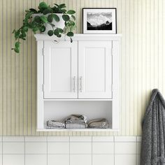 a bathroom with a white cabinet and green plant on the wall above it, next to a towel rack