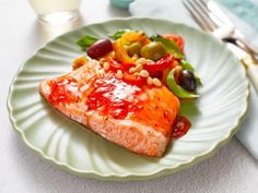 a piece of salmon on a plate with olives, peppers, and pine nuts