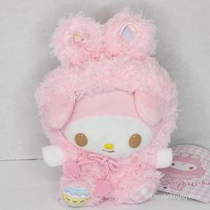 a pink teddy bear with fluffy fur on it's head and ears, sitting next to an egg