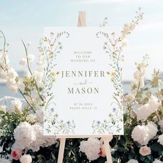 a welcome sign sitting on top of a wooden easel surrounded by flowers and greenery