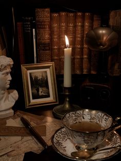 a table topped with books and a bowl filled with liquid next to a lit candle