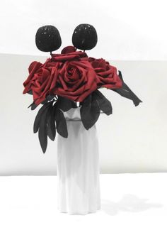 a white vase filled with red roses and two black balls sitting on top of it