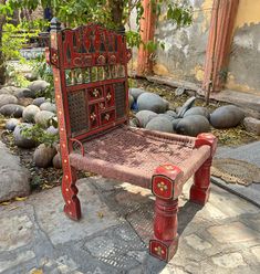 a red bench sitting on top of a stone floor next to a tree and rocks