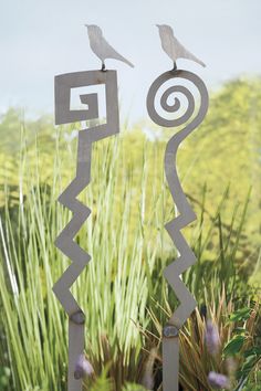 two birds are perched on top of some metal sculptures in front of grass and flowers