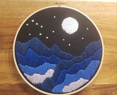 an embroidery project with mountains, stars and the moon in the sky on a wooden surface