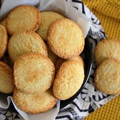 some biscuits are in a black bowl on a yellow and white cloth next to a cup of coffee