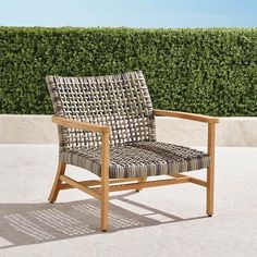 a wooden chair sitting on top of a cement floor next to a green hedge covered wall