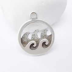 This beautiful ocean wave charms, crafted in an antique silver-tone finish, brings a calming coastal vibe to any jewelry piece. Featuring a circular frame with stylized waves and a textured design, this charm is perfect for nautical, beach-inspired, or bohemian accessories. Quality and versatile, it makes an excellent addition to necklaces, bracelets, or earrings, adding a touch of the ocean to your creations. Material : Nickel free and Lead free zamac metal, Antique Silver Plated Color: Antique Silver  Size : 30x25mm Calming Coastal, Wave Pendant, Ocean Inspired Jewelry, Circular Frame, Bohemian Accessories, Earring Charms, Jewelry Making Charms, Textured Design, Ocean Wave