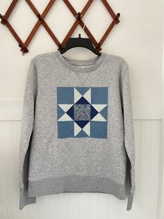 a gray sweater with a blue and white patchwork design hanging on a wooden hanger