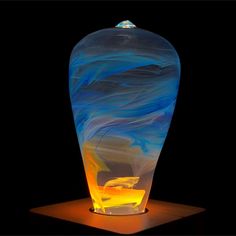 a glass vase sitting on top of a wooden table next to a black background with an orange and blue swirl in it