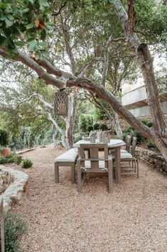 an outdoor table and chairs under a tree in the middle of a graveled area