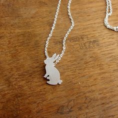 a silver rabbit necklace sitting on top of a wooden table