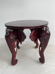 an elephant carved wooden table with two elephants on it's legs, sitting on a tile floor