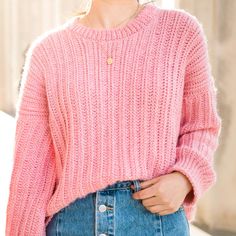 a woman wearing a pink sweater and denim skirt