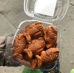 a person holding a plastic container filled with small carved animal cookies in it's palm