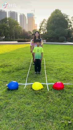 two children and an adult are standing in the grass with three colored balls on it