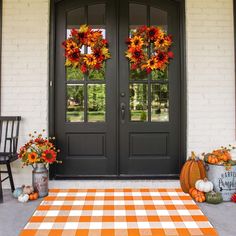 two wreaths on the front door of a house with pumpkins and gourds