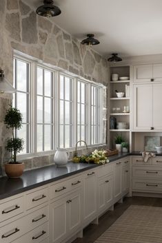 a large kitchen with white cabinets and black counter tops, along with a stone wall