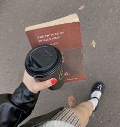 a person holding a coffee cup and a book in their hand while standing on the street