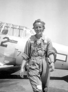 an old photo of a woman standing next to a plane on the tarmac with her hand in her pocket