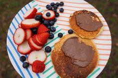 pancakes with chocolate frosting, strawberries and blueberries are on a paper plate