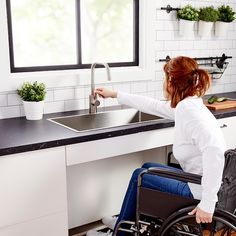 a woman in a wheel chair is washing her hands at the kitchen faucet