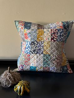 a decorative pillow and two small pumpkins on a black table with a white wall in the background