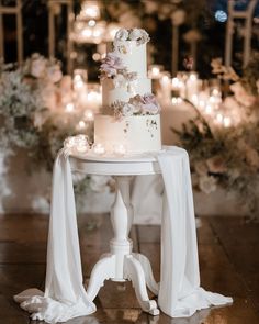 a white wedding cake sitting on top of a table with candles in the back ground