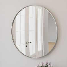 a round mirror hanging on the wall next to a vase with flowers